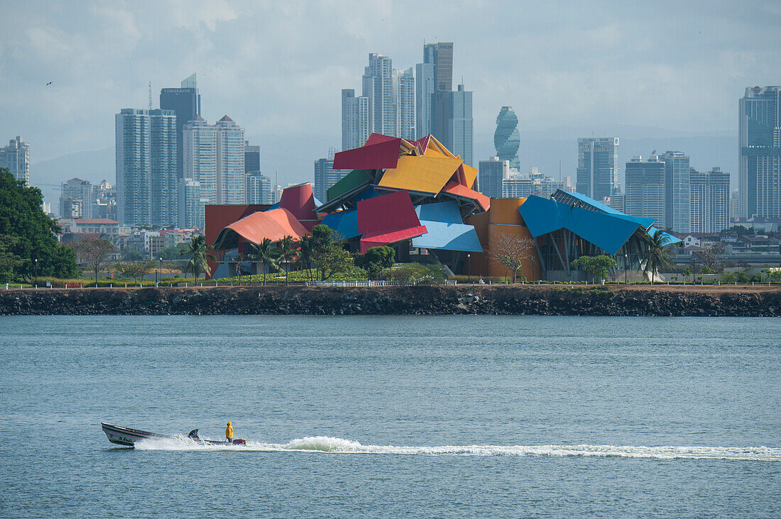 A power boat passes in front of the Panama City skyline featuring the colorful Biomuseo museum designed by Frank Gehry, Panama City, Panama, Central America