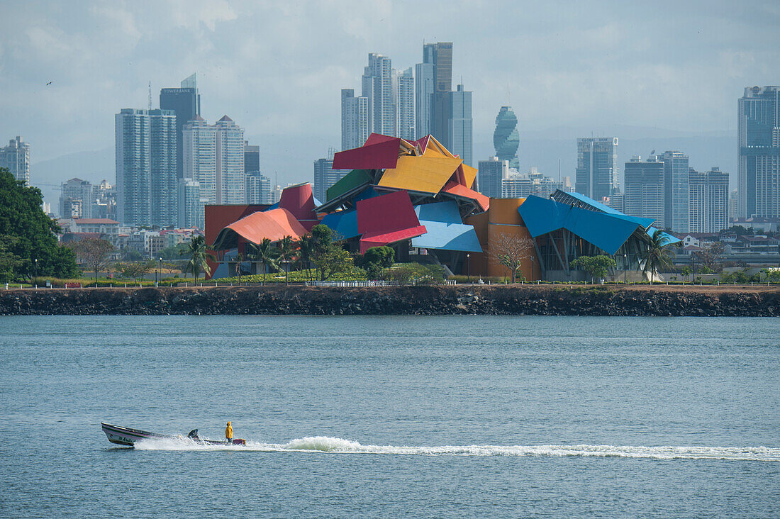 Ein Motorboot passiert die Skyline von Panama-Stadt mit dem bunten von Frank Gehry entworfenen Biomuseo Museum, Panama City, Panama, Mittelamerika