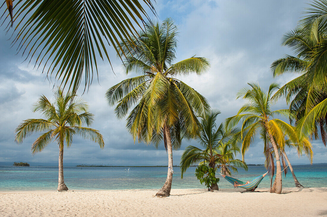 Ein Tagesbesucher von einem Expeditions-Kreuzfahrtschiff entspannt sich in einer Hängematte zwischen Palmen am Strand, San Blas-Inseln, Panama, Mittelamerika