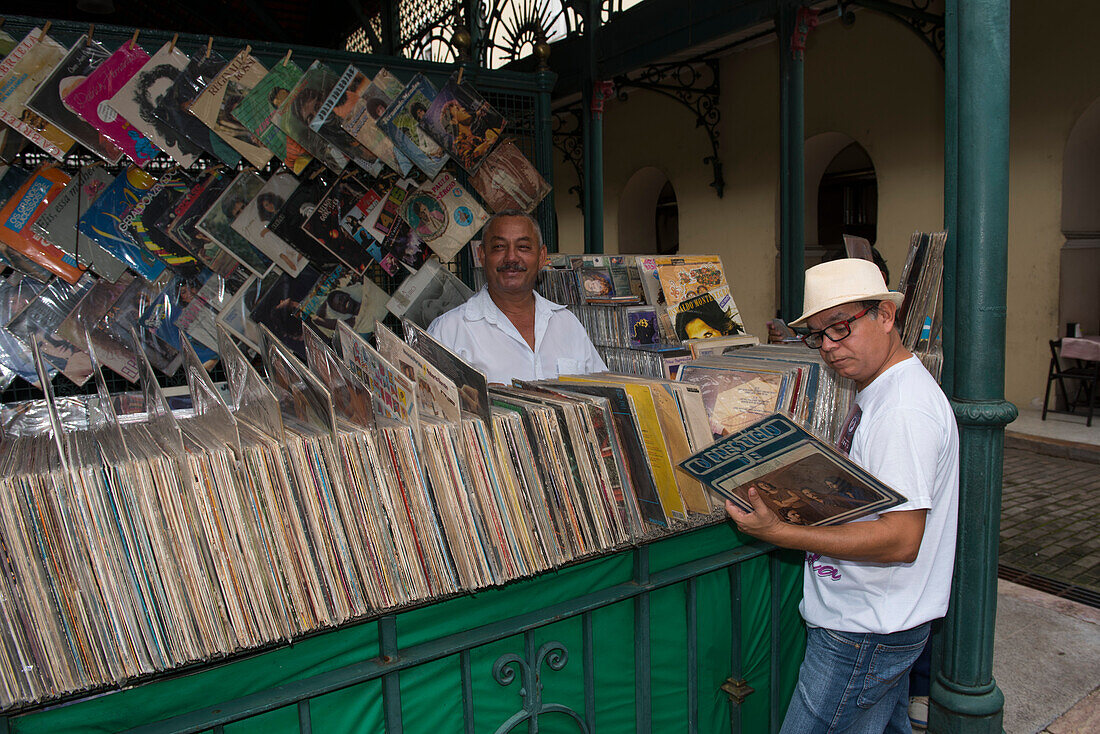 A salesman smiles into the camera while a customer searches for hidden treasures among the vinyl LP records, Belem, Para, Brazil, South America