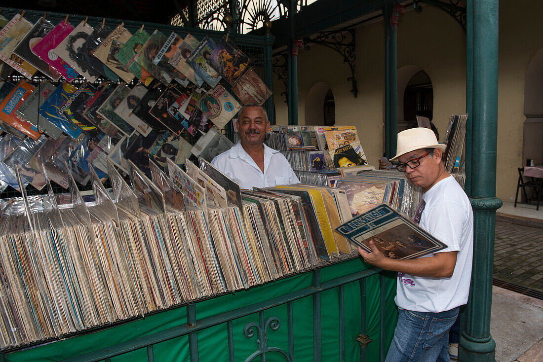 Ein Verkäufer lächelt in die Kamera während ein Kunde nach versteckten Schätzen unter den Schallplatten sucht, Belem, Para, Brasilien, Südamerika