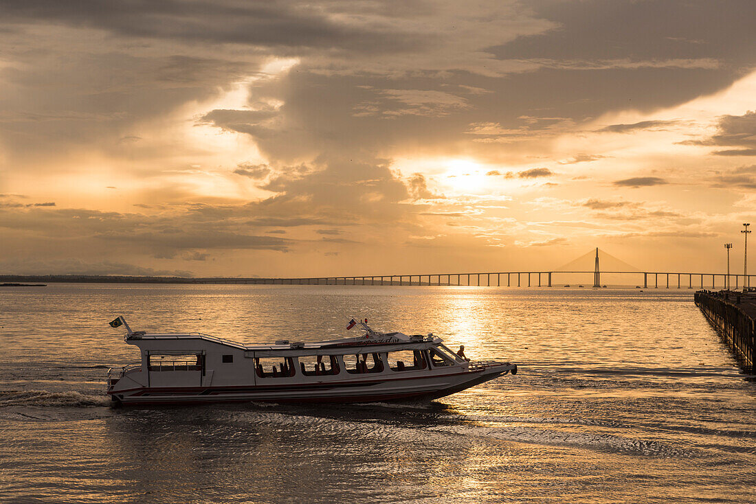 Kurz vor Sonnenuntergang nähert sich ein kleines Ausflugsboot dem Pier, im Hintergrund die Brücke Ponte Rio Negro, Manaus, Amazonas, Brasilien, Südamerika