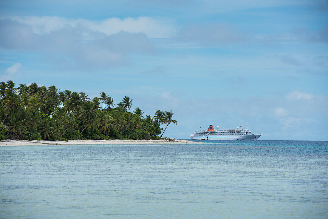 Expedition cruise ship MS Bremen (Hapag-Lloyd Cruises) lies offshore an island covered by palm trees and surrounded by white sand beaches and coral reefs, Likiep Atoll, Ratak Chain, Marshall Islands, South Pacific