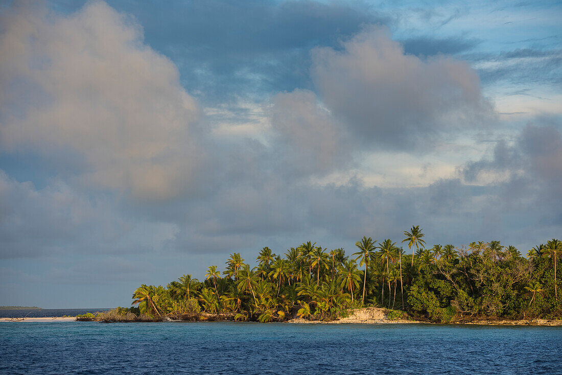 Late afternoon sun shines on a palm-covered island under lightly clouded skies, Likiep Atoll, Ratak Chain, Marshall Islands, South Pacific