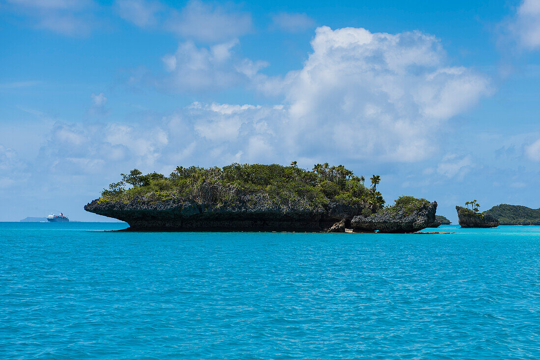Eine Gruppe von kleinen pilzförmigen Inseln, die mit Bäumen und Büschen bedeckt sind, erheben sich aus türkisfarbenem Wasser, wobei das Expeditions-Kreuzfahrtschiff MS Bremen (Hapag-Lloyd Kreuzfahrten) in der Ferne sichtbar ist, Fulaga Island, Lau Group, 
