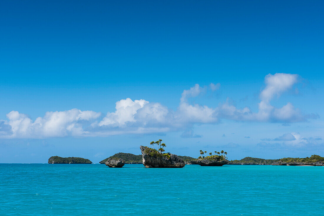Winzige, schroffe Inseln, einige mit Palmen gekrönt, stehen vor größeren Inseln im Hintergrund, die alle von türkisfarbenem Wasser umgeben sind, Fulaga Island, Lau Group, Fidschi, Südpazifik