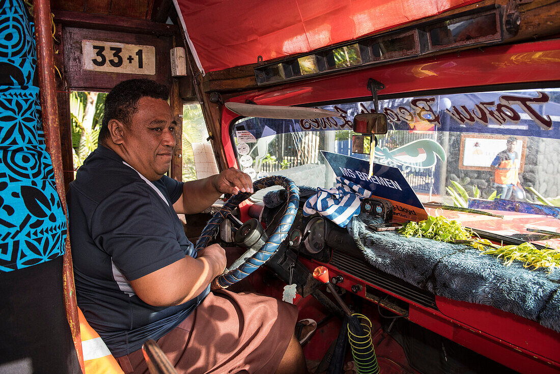 Ein Busfahrer, der das traditionelle Lavalava trägt, ein Rock-ähnliches Kleidungsstück, das von Männern und Frauen getragen wird, bereitet sich darauf vor, eine Gruppe von Expeditionsschiffpassagieren auf eine Exkursion zu fahren, Fagamalo, Savai'i, Samoa