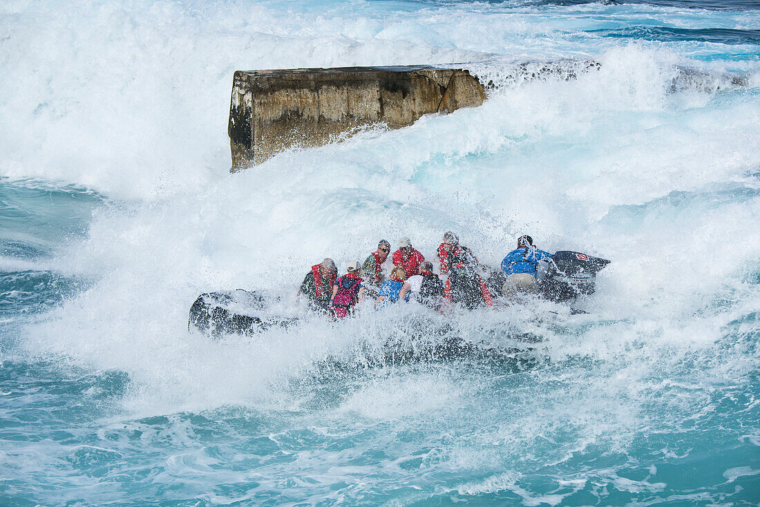 Die Passagiere eines Expeditions-Kreuzfahrtschiffes erhalten in ihrem Zodiac-Schlauchboot eine Ladung Wasser ab während Wellen um sie herum rollen, Atiu, Cookinseln, Südpazifik