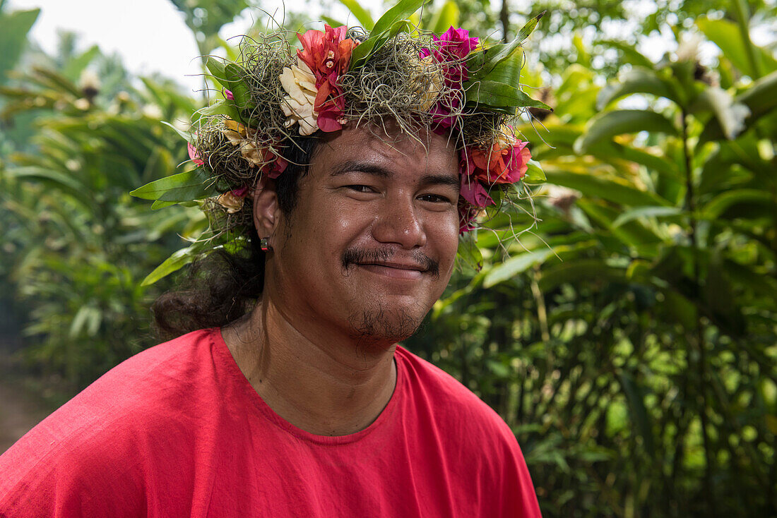 Ein junger Mann, der ein rotes T-Shirtt sowie einen Kopfschmuck aus Blumen, Blättern und Moos trägt, lächelt den Betrachter an, Rurutu, Austral-Inseln, Französisch-Polynesien, Südpazifik