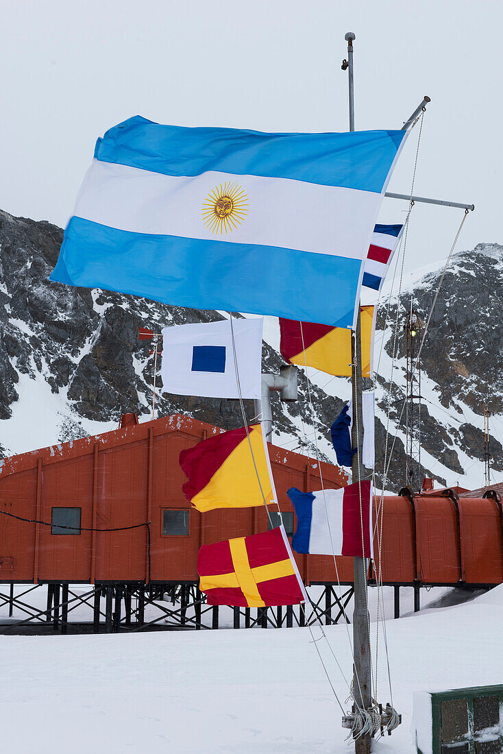 Die blau-weiße Flagge Argentiniens fliegt prominent vor Signalflaggen der Forschungsstation Base Orcadas, Laurie Island, Südliche Orkney-Inseln, Antarktis