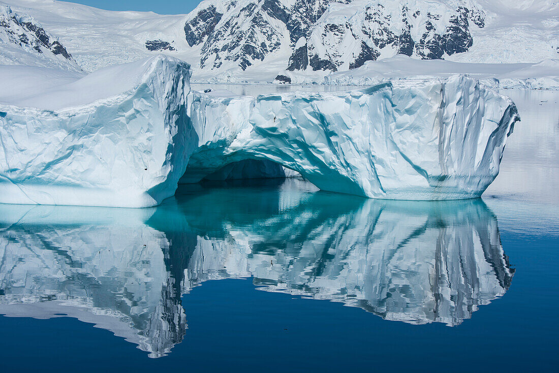 Ein seltener windstiller Moment erzeugt ein Spiegelbild einer Eisformation mit niedrigem Bogen, Wilhelmina Bay, Antarktische Halbinsel, Antarktis