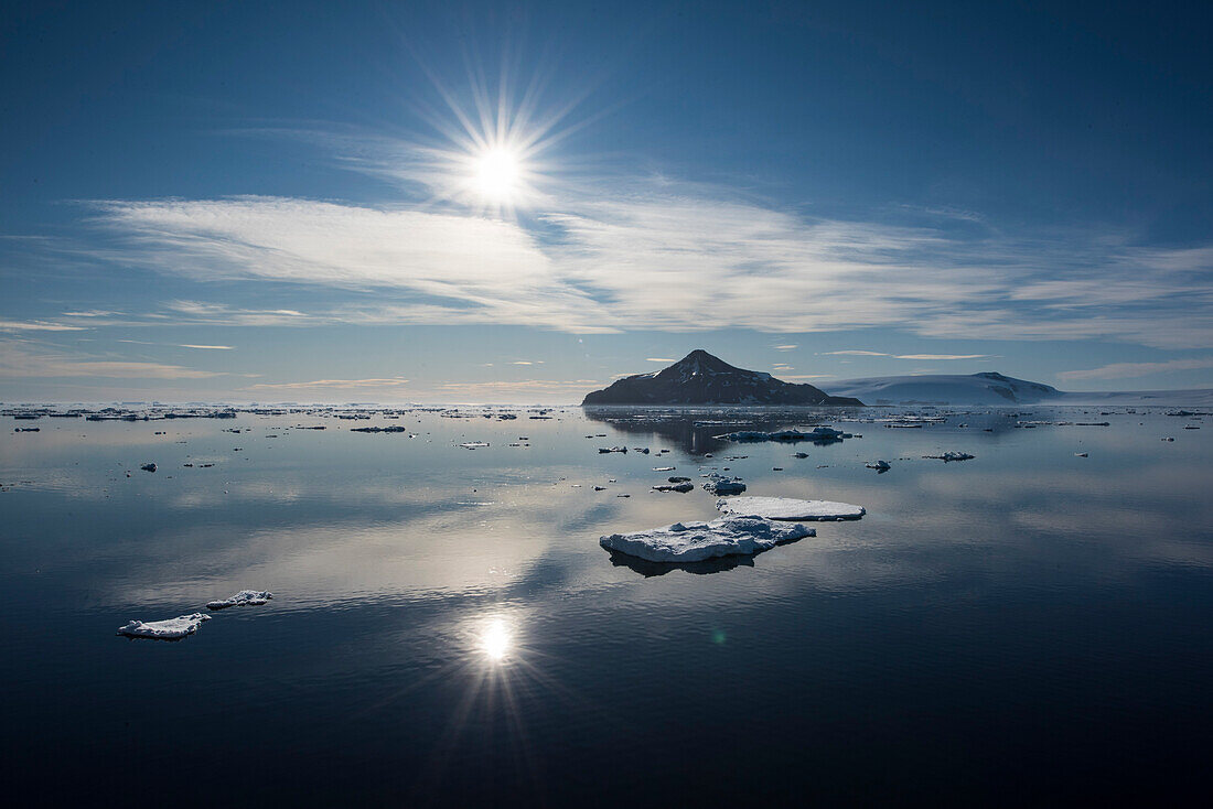 Eine strahlende Sonne scheint auf ein Meer mit ruhigem Wasser, Meereis und einer fernen Insel, Paulet Island, Antarktische Halbinsel, Antarktis