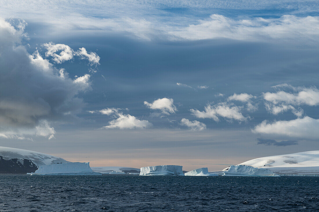 Dramatisches Licht verwandelt eine Szene mit schneebedeckten Inseln, Eisbergen und feinen Wolken in eine verträumte Landschaft, Brown Bluff, Weddell Sea, Antarktische Halbinsel, Antarktis