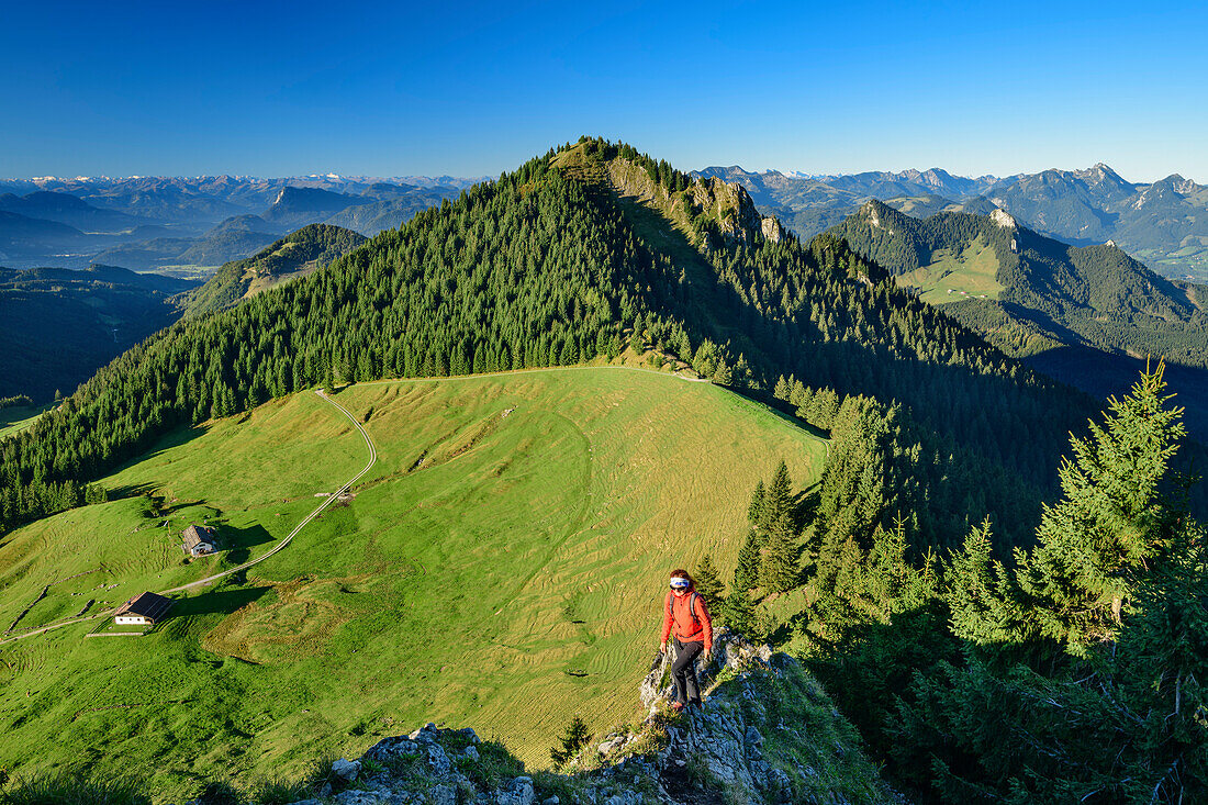 Woman hiking ascending on ridge towards Karkopf, alpine huts and Feichteck in background, Karkopf, Chiemgau Alps, Upper Bavaria, Bavaria, Germany