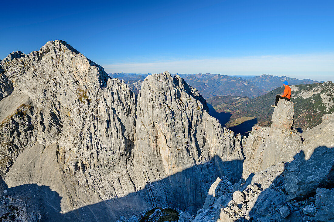 Man sitting on rock spire and looking towards rock wall of Hintere Karlspitze, from Hintere Goinger Halt, Wilder Kaiser, Kaiser range, Tyrol, Austria