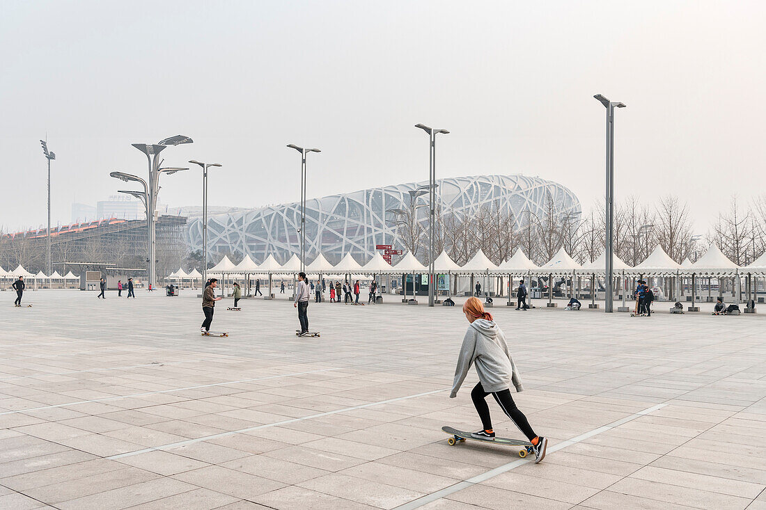 Junge Chinesen fahren mit Longboard vor sog. Vogelnest von Herzog & de Meuron, Nationalstadium, Smog, Olympischer Park, Peking, China, Asien