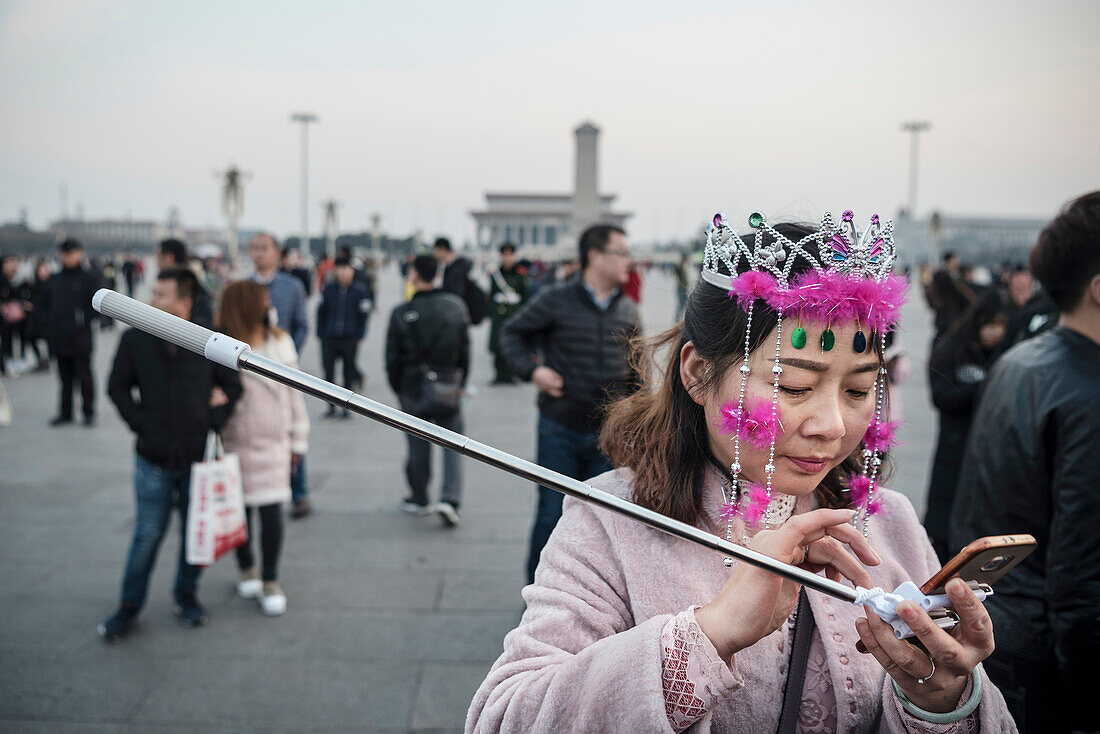Chinesin mit Selfie-Stick und pinkem Kopfschmuck bedient ihr Handy, warten auf Flaggen Zeremonie und Wachablösung am Platz des Himmlischen Friedens, Peking, China, Asien