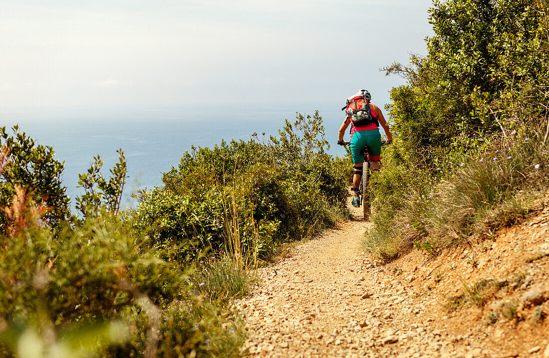 Junge Frau fährt mit dem Mountainbike auf einem Singletrail in Finale Ligure mit Blick auf das Mittelmeer, Italien