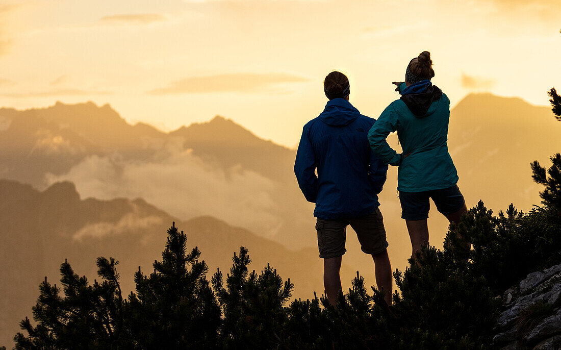 Junge Frau und junger Mann blicken bei Sonnenuntergang in die Ferne der Berglandschaft, Silhouette, Scharnitz, Karwendel, Tirol, Österreich