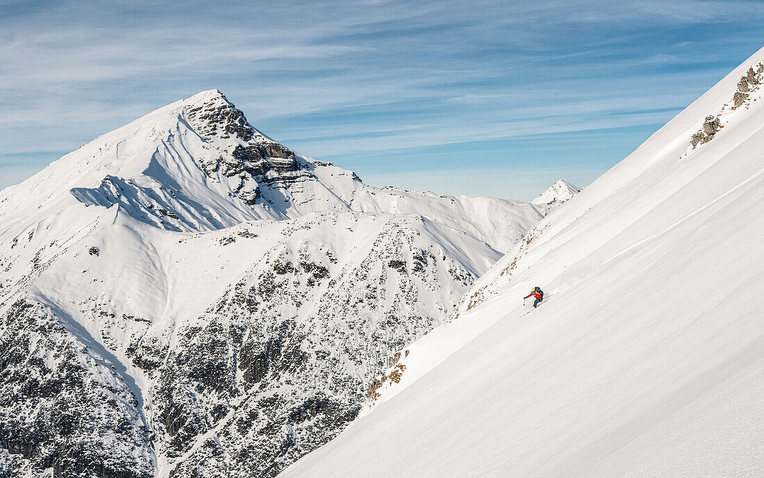 Skitourengeher fährt durch einen unberührten Tiefschneehang in den Lechtaler Alpen, Namlose Wetterspitze im Hintergrund, Lechtaler Alpen, Tirol, Österreich