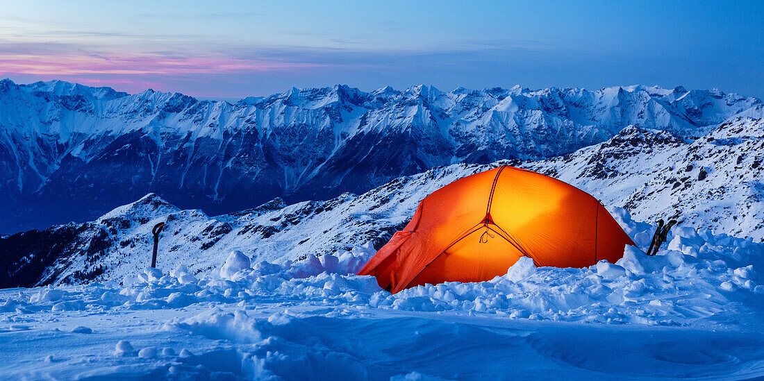 Orangfarbenes, leuchtendes Zelt im Schnee auf Gipfelhöhe bei Dämmerung, Innsbruck, Tirol, Österreich