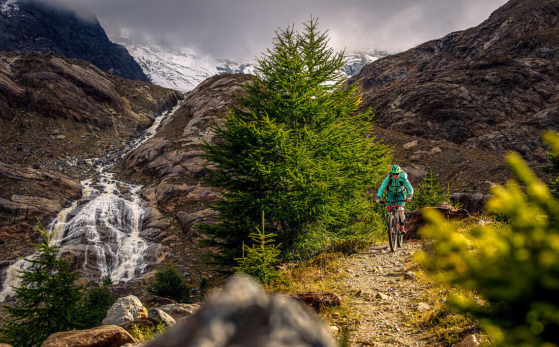 Young woman riding her mountainbike next to an alpine river, glacier in the background, Val Forni, Valfurva, Lombardia, South Tyrol, Italy