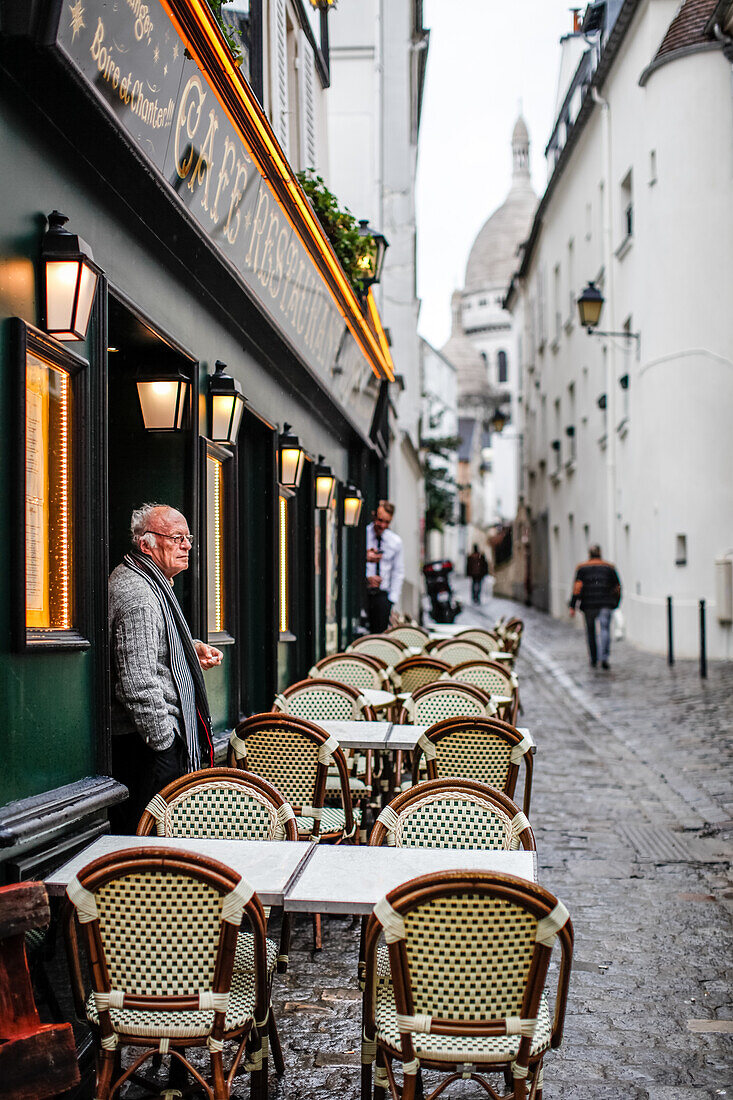 Ein alter Mann raucht vor dem Eingang in ein Restaurant und Basilika Sacre-Coeur in Montmartre, Paris, Frankreich, Europa