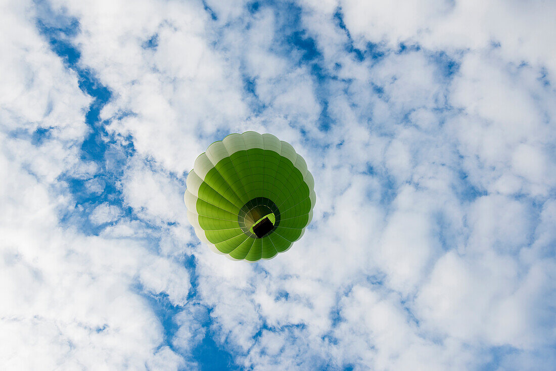 Grüner Heißluftballon vor blauem Himmel mit Wolken, Frankreich