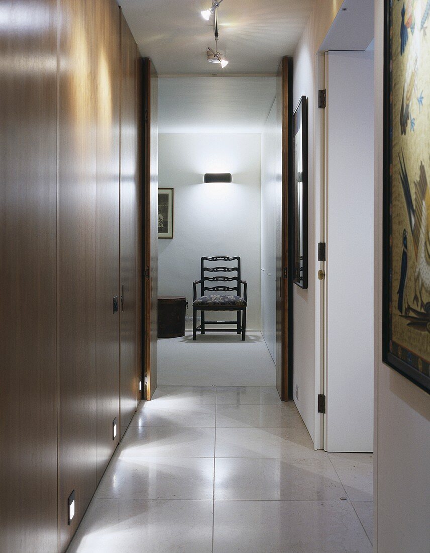 A modern hallway with built-in wooden cupboards and a view through an open door of a chair