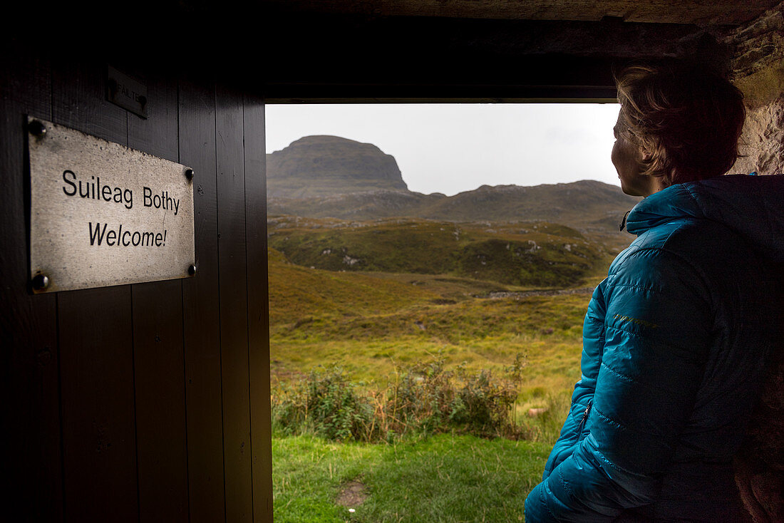Eine Wanderin blickt aus der Suileag Bothy, Inverpolly Nature Reserve, Highlands, Schottland, Großbritannien