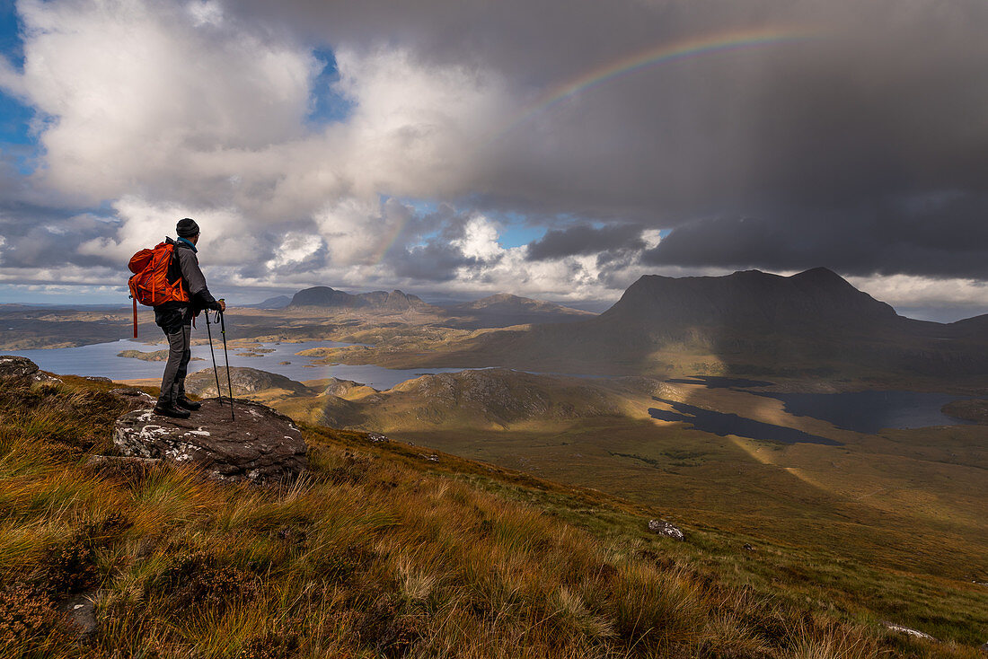 Hiker looks out from Stac Pollaidh on Loch Sionasgaig and Cul Mor, Inverpolly Nature Reserve, Highlands, Scotland, UK