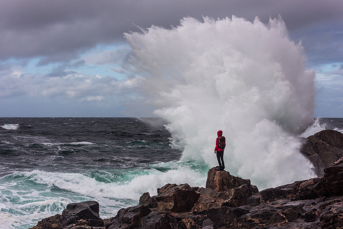 A woman is standing in front of the surf of the sea at Sheigra, waves breaking at the rock, Highlands, Scotland, UK