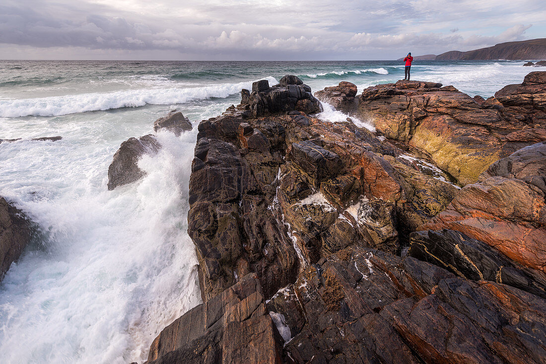 Ein Mann steht auf einem Felsen vor der Brandung an der Sandwood Bay, Highlands, Schottland, Großbritannien