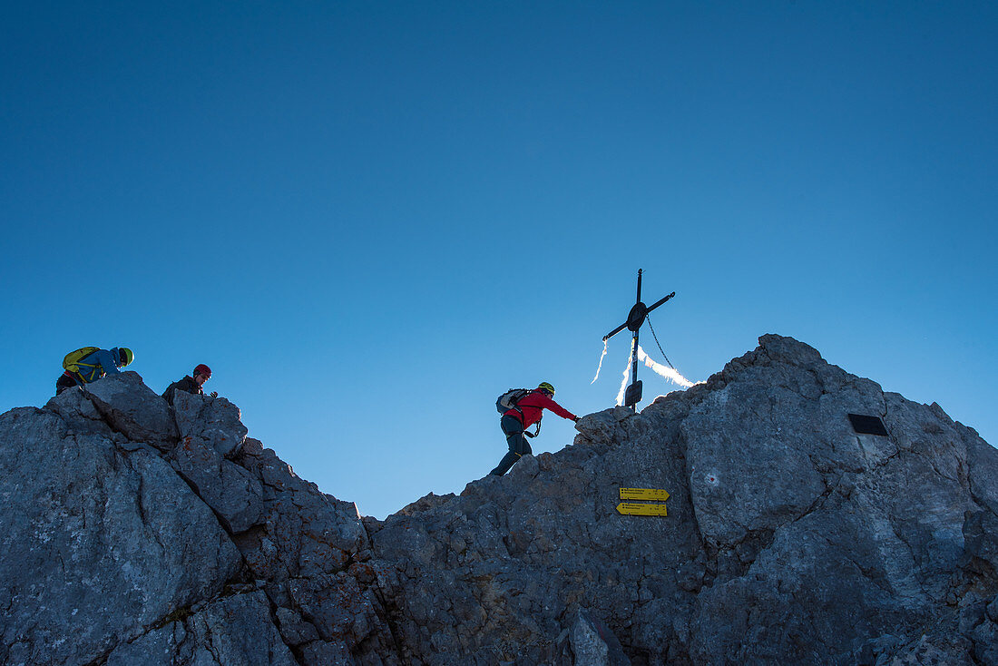 Bergsteiger bei Ankunft auf der Mittelspitze des Watzmann, Gipfelkreuz vor blauem Himmel, Berchtesgadener Alpen, Berchtesgaden, Deutschland