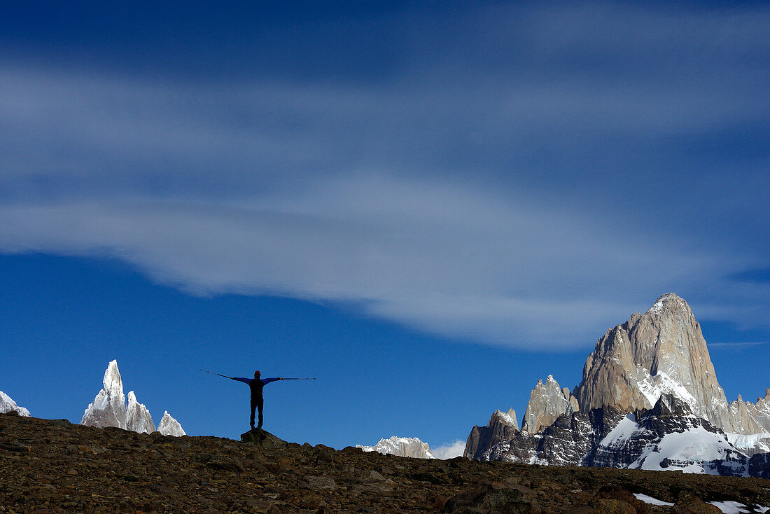 Ein Wanderer spreitzt seine Arme mit Treckingstöcken, Fitz Roy & Cerro Torre im Hintergrund, Nationalpark Los Glaciares, Patagonien, Argentinien