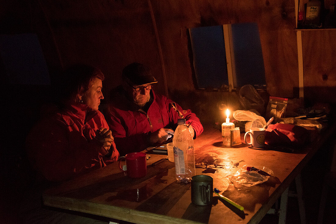 Ein Paar am Tisch im Inneren des Refugio Garcia Soto (Chile) bei Kerzenlicht, Nationalpark Los Glaciares, Patagonien, Argentinien