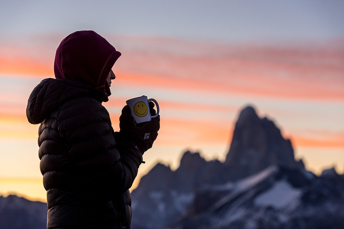 Eine Wanderin trinkt Kaffee vor der morgendlichen Silhouette des Fitz Roy, Nationalpark Los Glaciares, Patagonien, Argentinien
