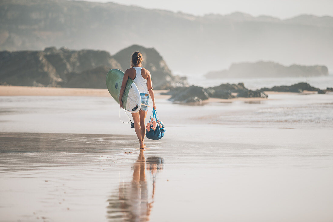 Eine Frau mit Surfbrett an der Küste Nordspaniens läuft am Strand entlang