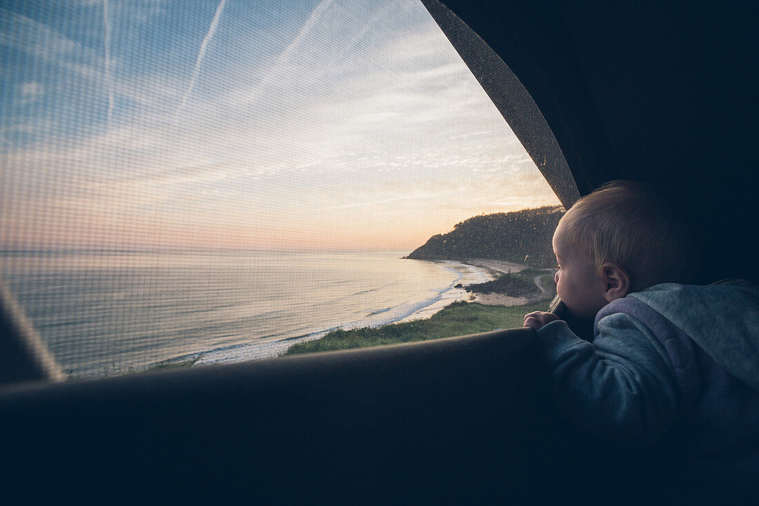 Toddler looks out of a tent on the coast of northern Spain