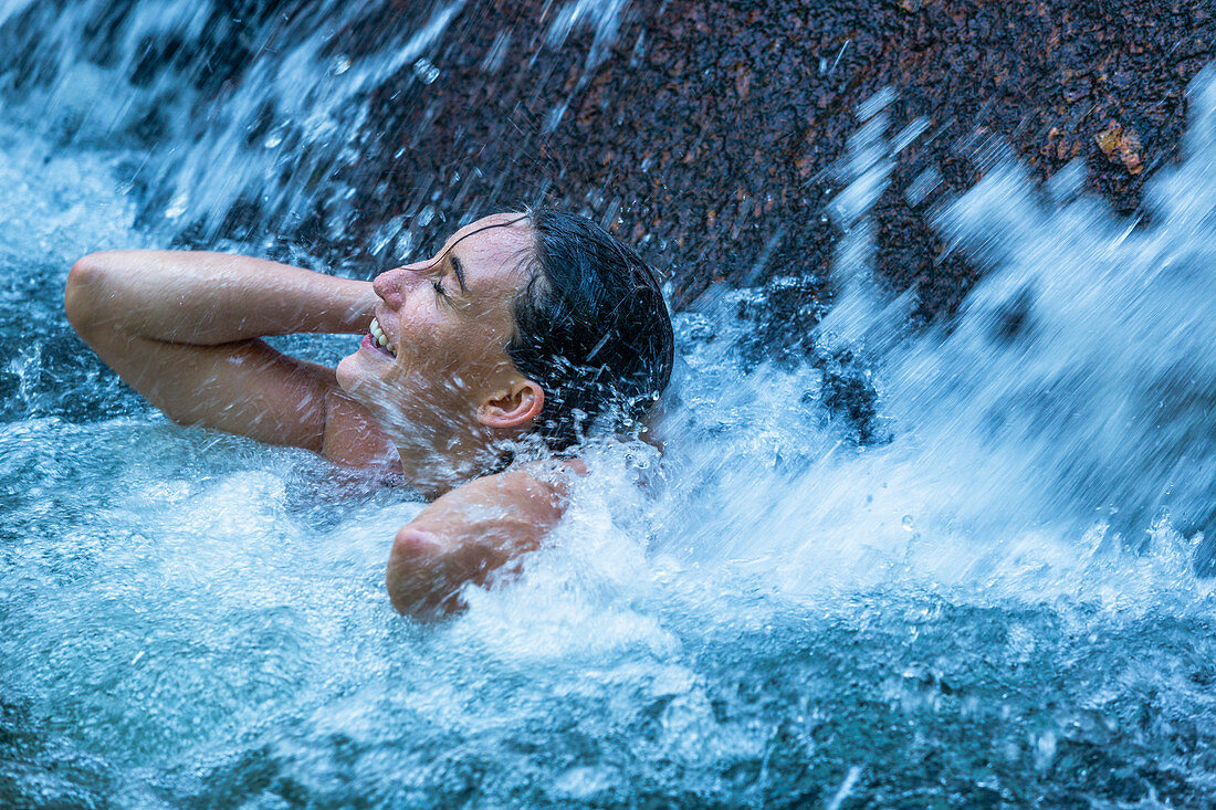 Eine Frau erfrischt sich unter einem Wasserfall in Phuket, Thailand