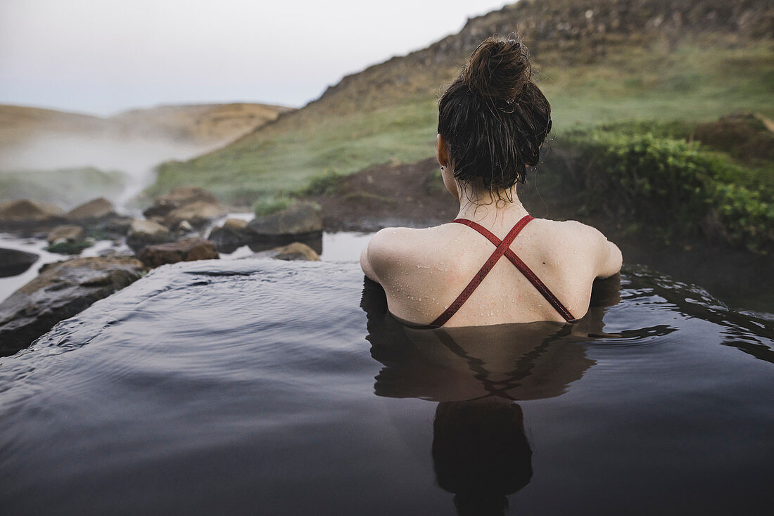 Junge Frau sitzt in einem Becken mit heißem Wasser, Island