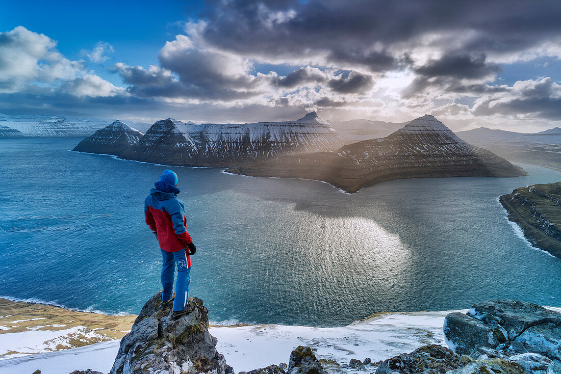 Hiker on rocks admiring the rays of sun over Funningur fjord, Eysturoy island, Faroe Islands, Denmark