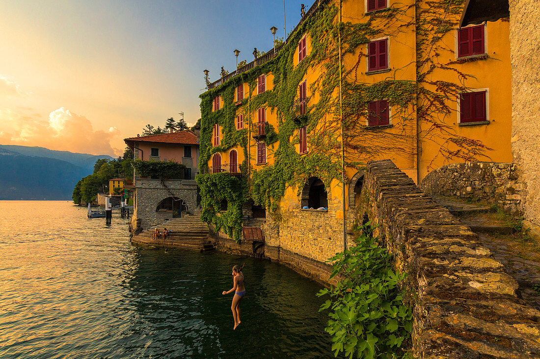 Girl dives into the lake from a bridge during sunset. Nesso, Province of Como, Como Lake, Lombardy, Italy, Europe.