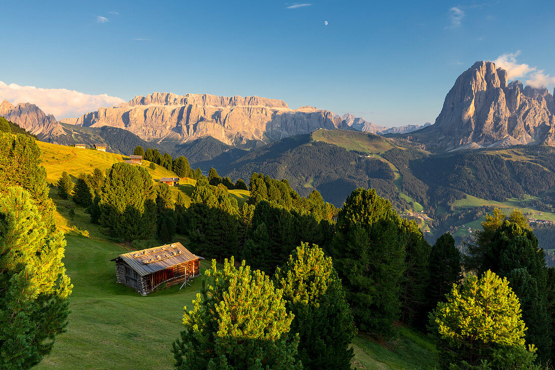 Last rays of sun on traditional hut with view on Sassolungo and Sella Group. Gardena Valley, South Tyrol, Dolomites, Italy, Europe.
