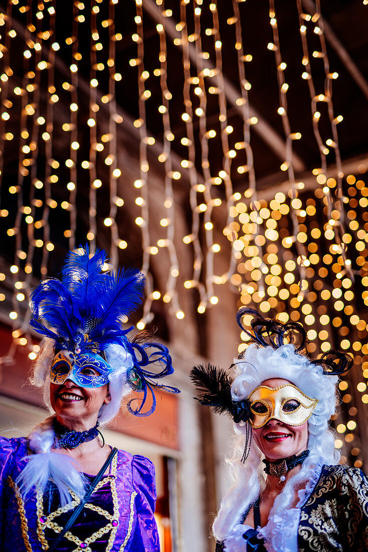 Women in costume and mask at the Venice Carnival 2019, lights and bokeh in background. Venice, Veneto, Italy
