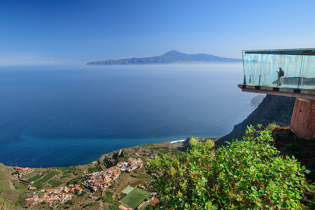 Person standing in glass skywalk with view to village of Agulo and Teneriffa with Teide, UNESCO World Heritage Teide, from Mirador de Abrante, La Gomera, Canary Islands, Canaries, Spain