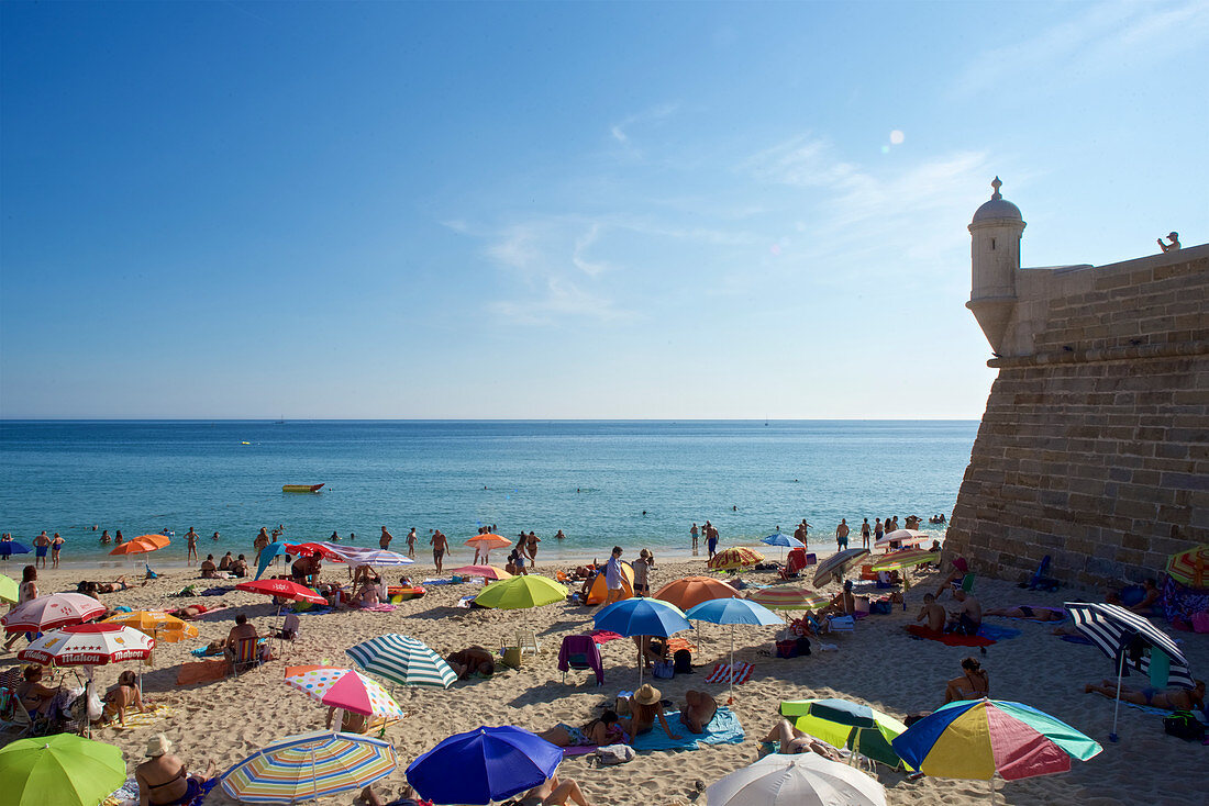 People on the beach next to the fortress in Sesimbra on the Setubal Peninsula, south of Lisbon, Portugal