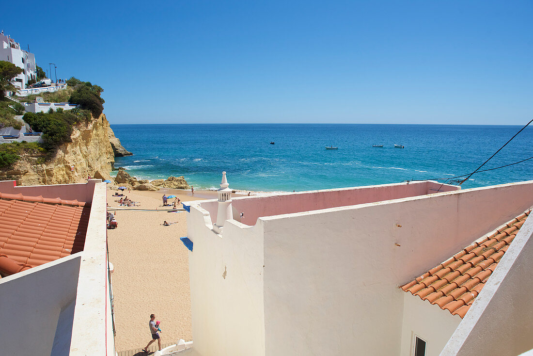 Blick zwischen Häusern zum Strand bei strahlend blauem Himmel in Carvoeiro, Lagoa, Algarve, Portugal