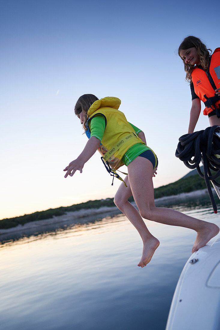 2 girls jump aboard a sailboat with life jackets, Bay of Tomozina, Cres, Croatia