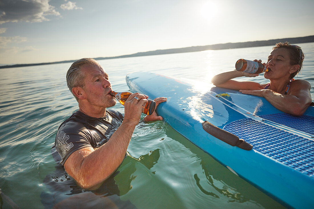 Pause am SUP Board, Mann und Frau trinken Bier im Starnberger See, Bayern, Deutschland